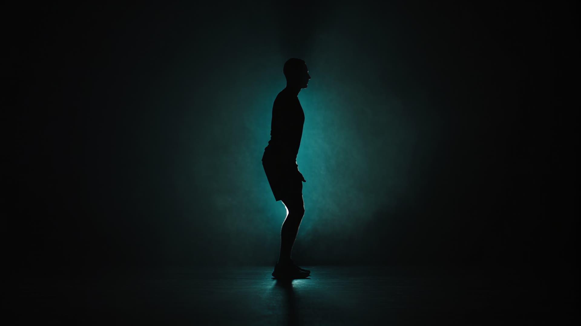 The silhouette of an athlete rising from a lunge, backlit in cyan haze on a dark studio floor