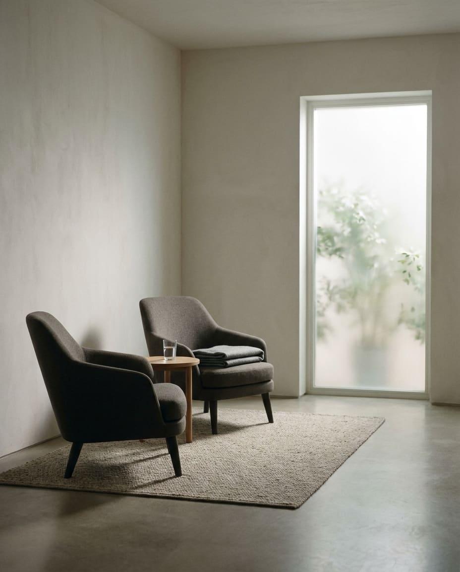Two armchairs angled toward each other beside a frosted window, a side table with a glass of water