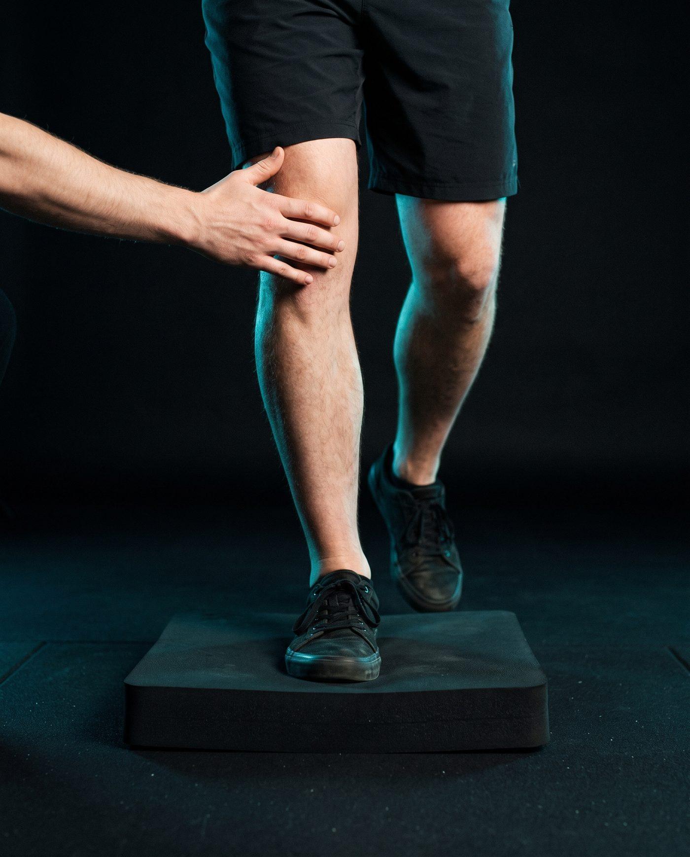 A lower leg stepping onto a balance pad with a clinician’s hands at the knee