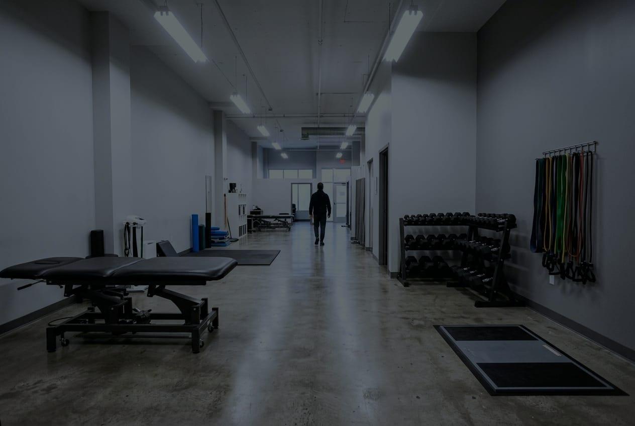 A long, bright rehabilitation floor with a treatment table, dumbbells and bands on the wall